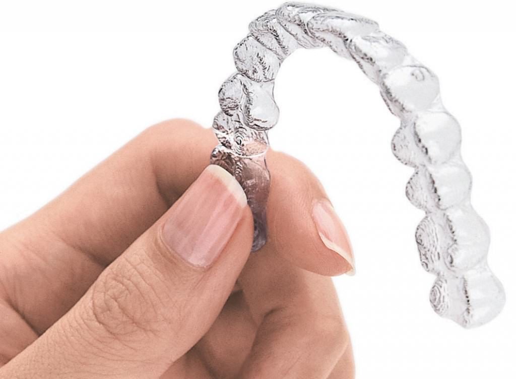 Invisalign aligner held in hand on white backdrop