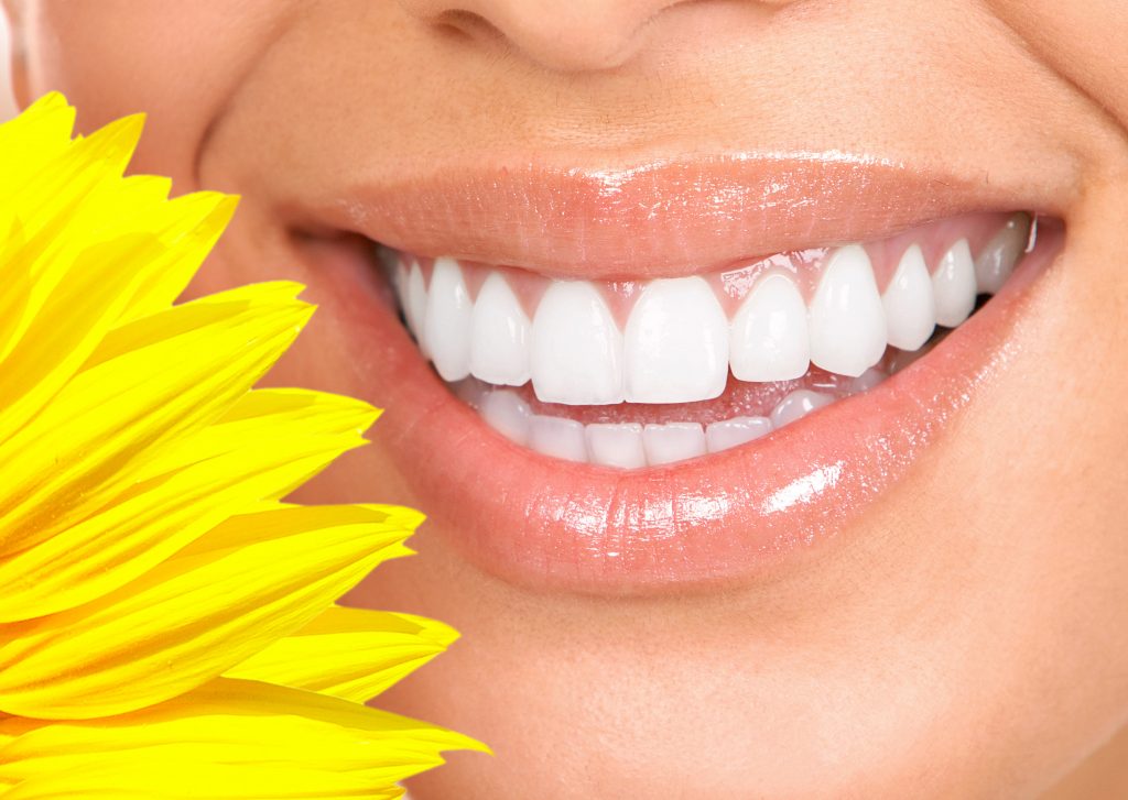 close up of woman's smile with a yellow flower