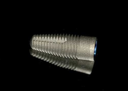 A dental implant screw over a black backdrop 