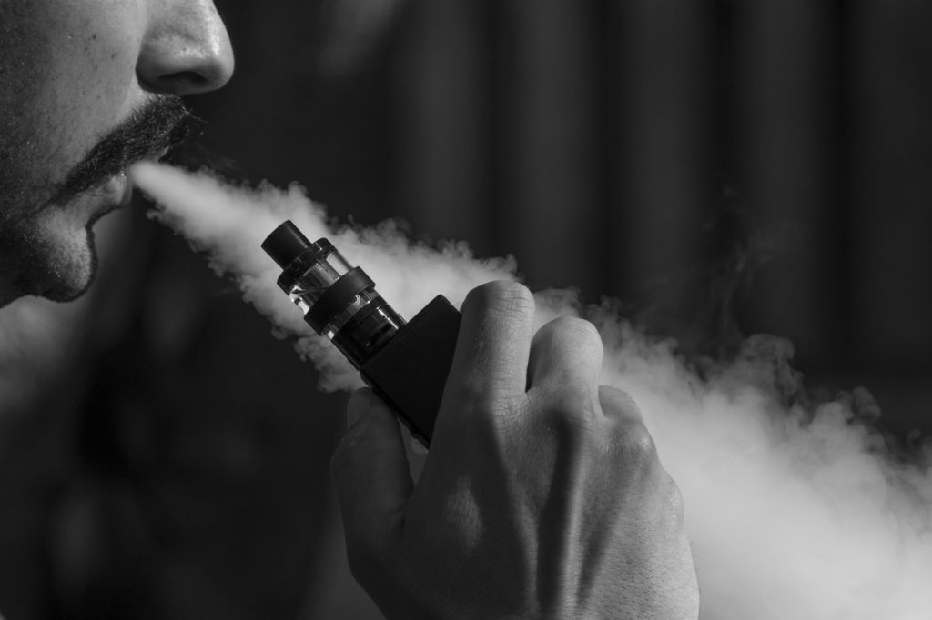A man blowing smoke while vaping black and white image