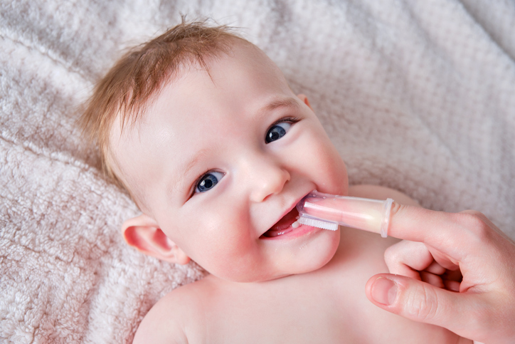 mother using finger brush to clean baby's teeth