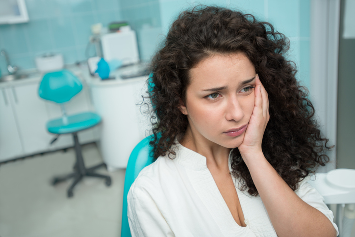 young woman holding her cheek at the dental office during a dental emergency