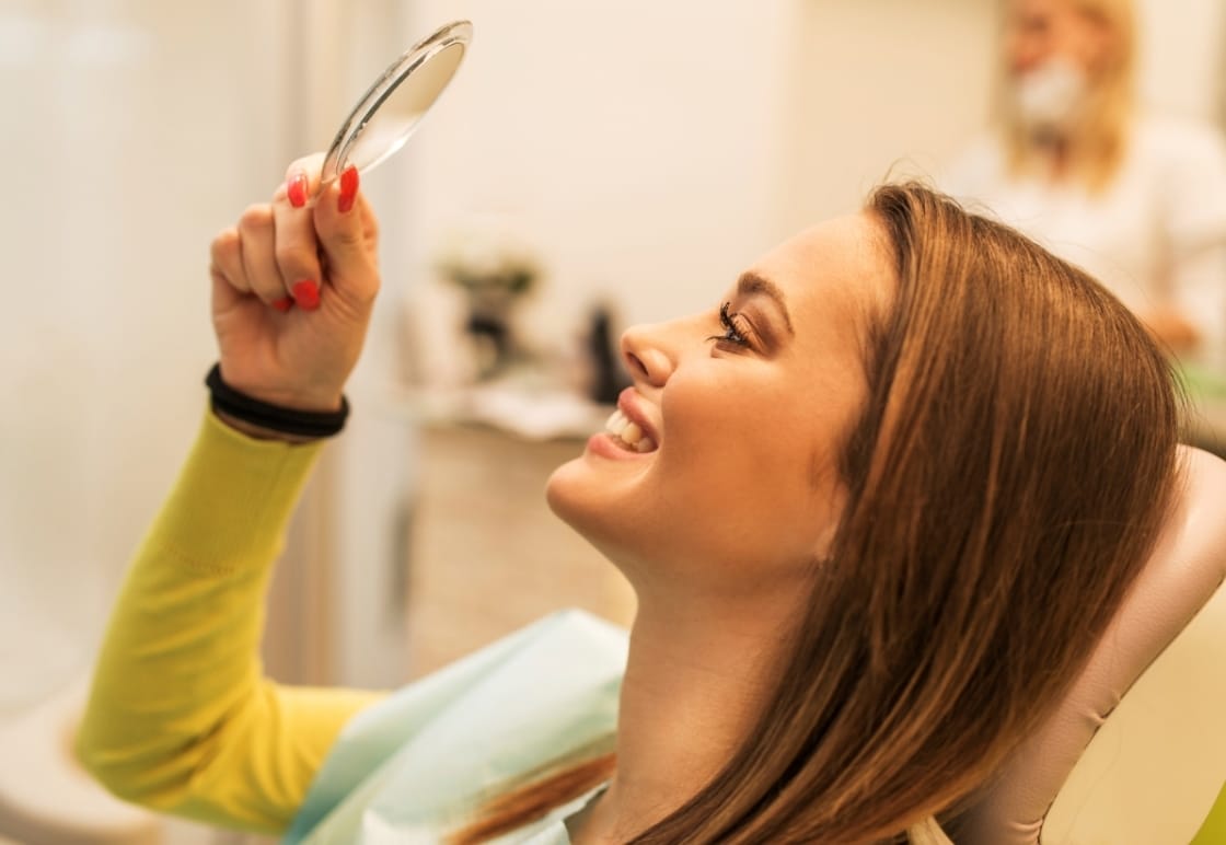 Woman in dental chair smiling and looking at hand mirror