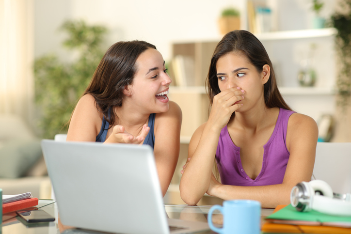 A woman with bad breath is talking to a friend who is covering her nose