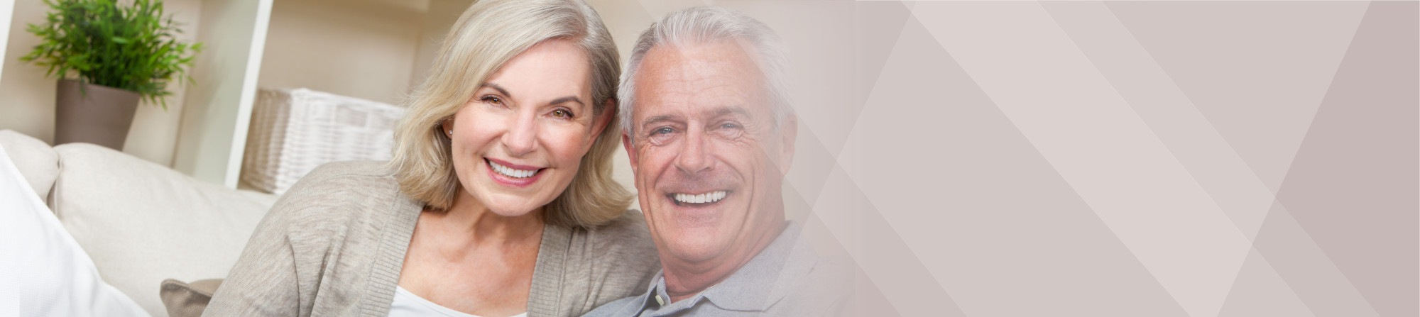 An older couple smiling while sitting on their couch.