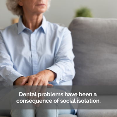 Elderly woman sitting alone on a couch. Caption: Dental problems have been a consequence of social isolation.