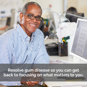 Man smiling at office desk. Caption: Resolve gum disease so you can get back to focusing on what matters to you.
