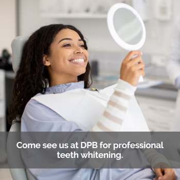 Woman admiring her teeth whitening procedure in a hand mirror at dental office.