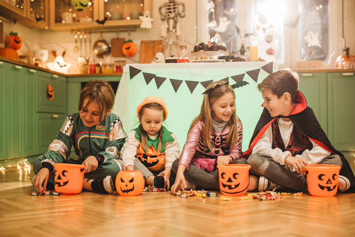 Four kids in costumes on the floor picking out the candy they like from their Halloween baskets