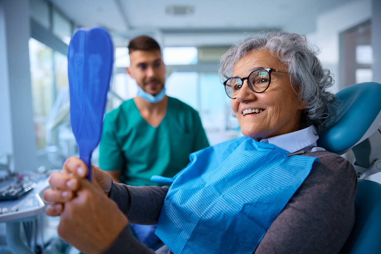 Woman at dental office with snap-on dentures looking in mirror, dentist in background