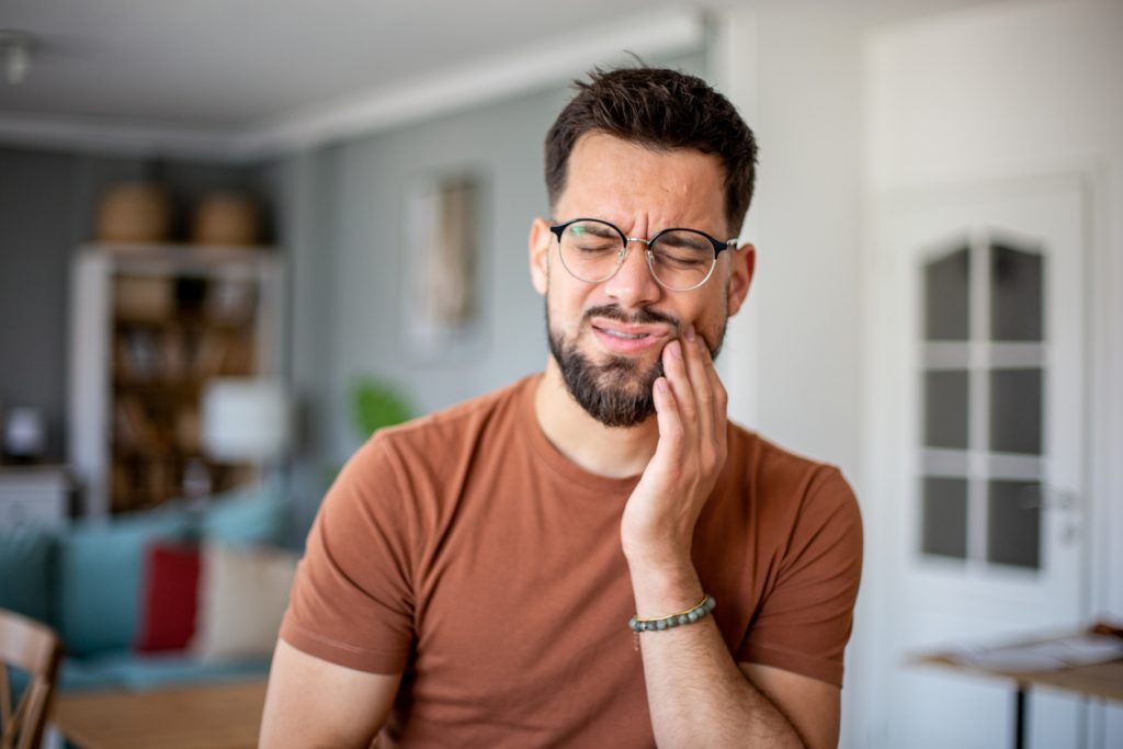 A man suffering from a toothache, touching his cheek at home