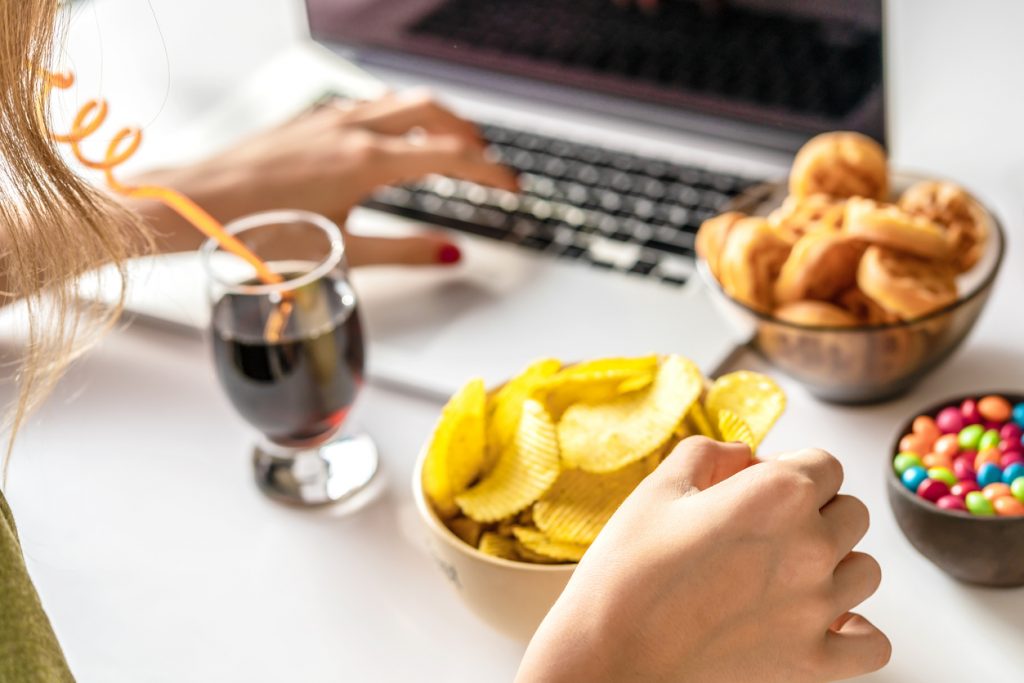 A woman is working on a laptop while snacking